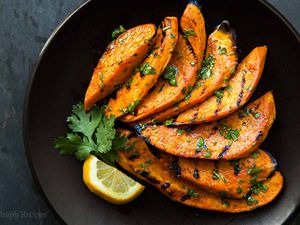 Grilled Sweet Potatoes on a dark plate with cilantro and lime garnish