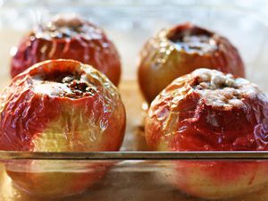 Four baked apples with their tops cut off and resting in a glass baking dish