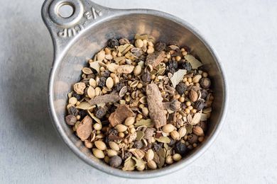 Pickling spice in a measuring cup: cinnamon, bay leaves, yellow mustard seeds, coriander seeds, black peppercorns, dill seeds, alspice berries, red pepper flakes