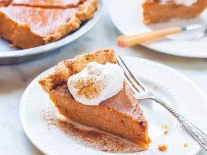 Slice of sweet potato pie on a white plate with whipped cream dusted with cinnamon and fork.