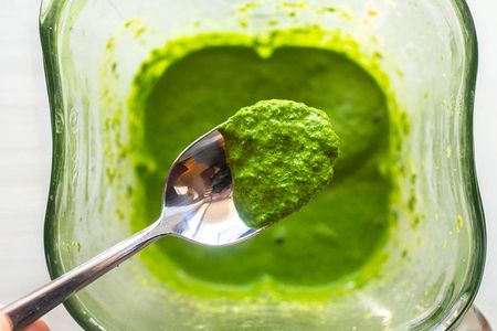Top view of a spoon with kale pesto on it. The spoon is above a blender jar with more pesto inside.