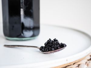 Spoonful of Fermented Elderberries on a Counter with the Syrup in a Bottle in the Background