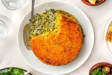 Sabzi Polo (Persian Herb Rice) on a Plate With a Serving Spoon, and Surrounding It, Small Plates With Sides and Glasses of Water 