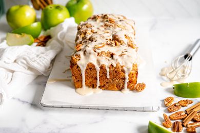 Apple Fritter Bread on Parchment Paper Surrounded by Granny Smith Apples, Pecans, and Sticks of Cinnamon