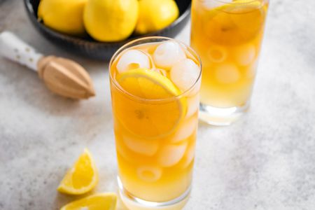 Two Glasses of Arnold Palmer With a Lemon Slice, Next to a Bowl of Lemons, a Citrus Reamer, and Lemon Wedges