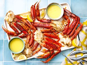 Tray of Easy Baked King Crab Legs With Bowls of Melted Butter and Lemon Wedges, and on the Counter Next to It, a Few Seafood Picks and Cracker on a Table Napkin