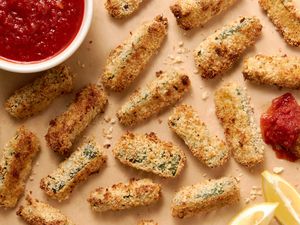 Baked Zucchini Fries on the Counter (One Was Dipped in Marinara Sauce), a Bowl of Marinara Sauce, and Lemon Wedges