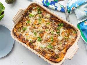 Beef Enchilada Casserole in a Casserole Dish Next to a Table Cloth, a Plate, and a Bowl with Side Salad 