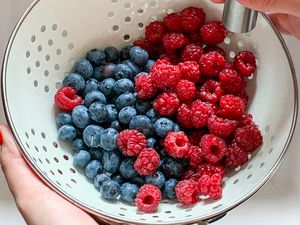 Hands holding a colander as they rinse strawberries and blueberries