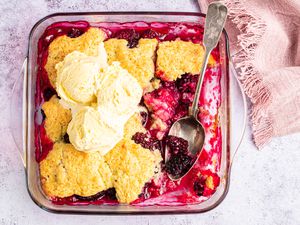 Overhead view of a baking dish with a serving removed from the blackberry cobbler and with a couple scoops of vanilla ice cream on top.
