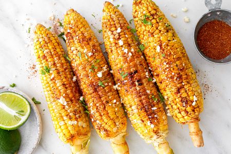 Cajun-Spiced Grilled Corn Next to a Saucer with Two Lime Halves and a Small Bowl with More Cajun Seasoning
