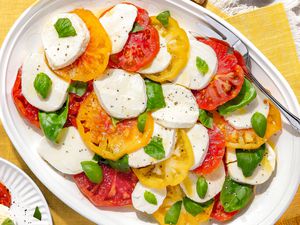 Platter of Caprese Salad With Tomatoes, Basil, and Mozzarella Next to a Plate With a Serving, All on a Yellow Placemat