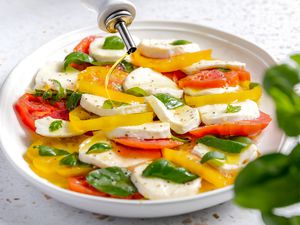 Olive Oil Drizzled Onto Platter of Caprese Salad With Tomatoes, Basil, and Mozzarella, and in the Foreground, a Basil Plant