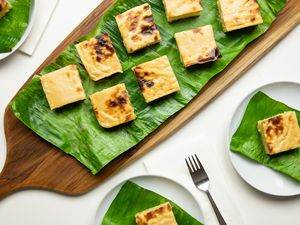 Aerial Shot: Cassava Cake Slices on a Banana Leaf Covered Wooden Tray, and Individual Slices of Cake on Banana Leaf Covered Plates