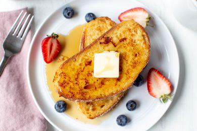 Challah French Toast with Butter, Fruit, and Syrup Surrounded by a Fork and Napkin