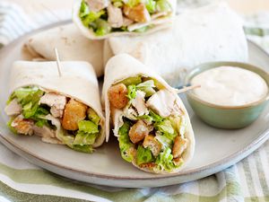 Chicken Caesar Wraps Cut in Half on a Plate with a Small Bowl of Dressing