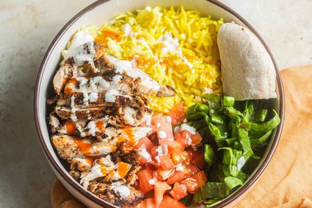 Bowl of Halal Cart-Style Chicken Over Rice Next to an Orange Kitchen Linen