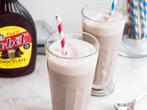 Egg Cream in Two Glasses with Bottle of Chocolate Sauce and Container of Straws in Background