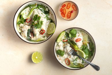 Overhead view of two bowls of Coconut poached cod with ginger and lime served with lime and rice.