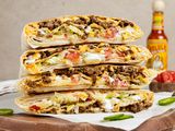 Stack of Copycat Crunchwrap Supreme Cut in Half on Parchment Paper Over a Wooden Board