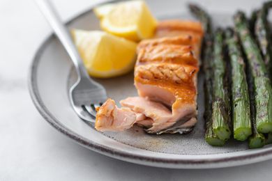 Grilled salmon with a forkful taken out alongside asparagus and lemon on the plate.