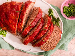 Easy Meatloaf With Some of It Cut Into Slices on a Platter and Sitting on a Sage Table Napkin Next to a Small Bowl With Sliced Parsley