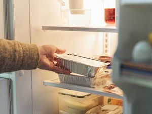 A hand reaching into a refrigerator to grab a takeout container