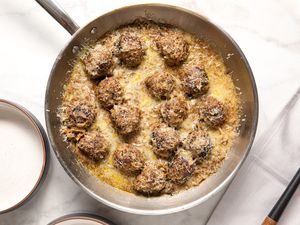 French Onion Meatballs in a Pan Next to Two Bowls and a Spoon on Table Cloth