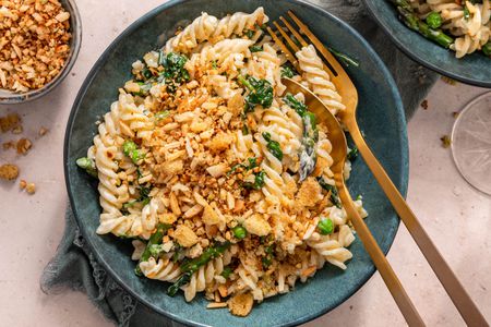Bowl of Fusilli With Spring Vegetables and Breadcrumbs Next to a Glass, a Bowl of Breadcrumbs, and a Another Bowl of Pasta