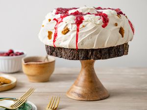 Gingersnap Pavlova with Cranberry Sauce Sitting on a Wooden Cake Stand, Surrounded by a Bowl of More Sauce, a Bowl with Cranberries, and a Plate with Gingersnaps