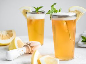 Glasses of Grapefruit Shandy Garnished with Mint and Grapefruit Wedge Surrounded by Grapefruit Wedges and Citrus Reamer