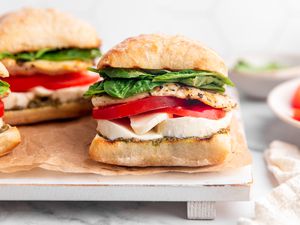 Grilled Chicken Caprese Sandwiches on a Parchment Lined Tray, and on the Counter Next to the Tray, Plates With Individual Ingredients 
