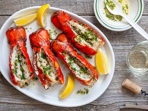 Platter of Grilled Lobster Tails with Lemon Wedges Surrounded by a Bowl of Garlic Herb Butter and a Glass
