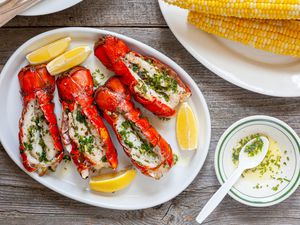 Platter of Grilled Lobster Tails with Lemon Wedges Surrounded by a Bowl of Garlic Herb Butter and a Plate of Corn 