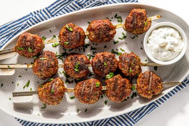 Platter of Grilled Meatballs With a Small Bowl of Tzatziki, All on a Blue and White Stripped Kitchen Towel