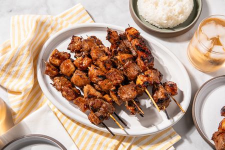 Grilled pork skewers on a white platter with rice on the side