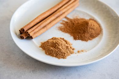 Mounds of cinnamon and cinnamon sticks on a white plate