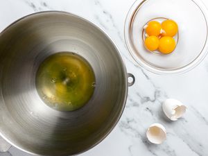 In One Large Bowl, Egg Whites, and Next to It, a Smaller Bowl With Egg Yolks. The Shells on the Counter.