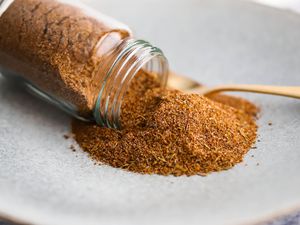 Jerk Seasoning Cascading From a Small Jar Onto a Plate With a Spoon for Jerk Spice Seasoning Recipe