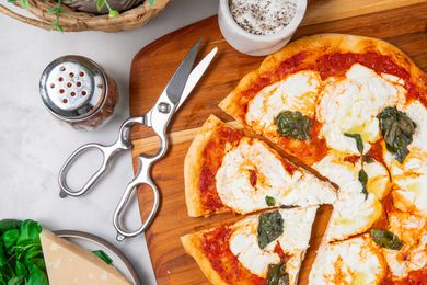 Kitchen shears alongside a partially sliced margherita pizza on a cutting board