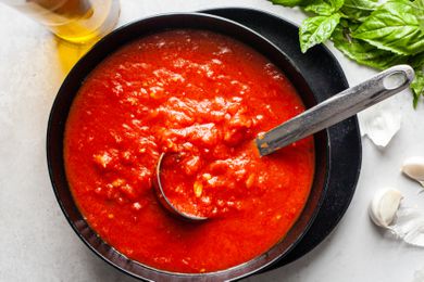 Bowl of Homemade Marinara Sauce With a Ladle, and in the Surroundings, a Bottle of Olive Oil, Garlic Cloves, and Fresh Basil Sprigs
