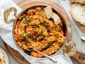 Menemen (Turkish Scrambled Eggs and Tomatoes) in a Pot with a Spoon, Surrounded by Some Slices of Bread and a Plate