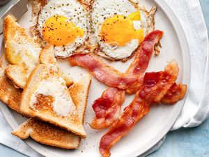 Cooked bacon on a plate with buttered toast and fried eggs