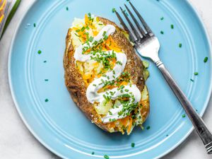 Microwave Baked Potato Topped with Sour Cream, Cheddar, and Chives on a Plate with a Fork