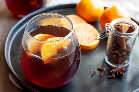 Stemless Wine Glass with Mulled Wine and Orange Slices on a Black Tray with Mandarin Orange Slices, Mandarin Oranges, and a Jar of Mulling Spices