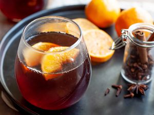 Stemless Wine Glass with Mulled Wine and Orange Slices on a Black Tray with Mandarin Orange Slices, Mandarin Oranges, and a Jar of Mulling Spices