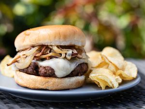 Side view of a mushroom and swiss burger on a plate with chips outside.