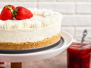 Side view of a A cake stand with no bake cheesecake topped with fresh strawberries.