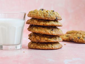 Stack of Oatmeal Banana Cookies Next to a Glass of Milk, and in the Background, More Cookies on the Counter