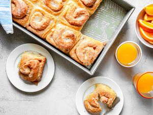 Orange Breakfast Rolls in a Baking Pan and on Small Plates Next to Glasses of Orange Juice and a Bowl of Orange Slices